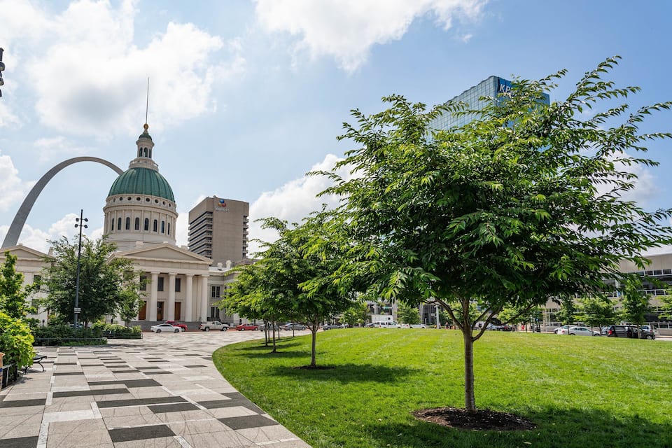 A city square with a large green dome building, a checkered pathway, and surrounding trees.