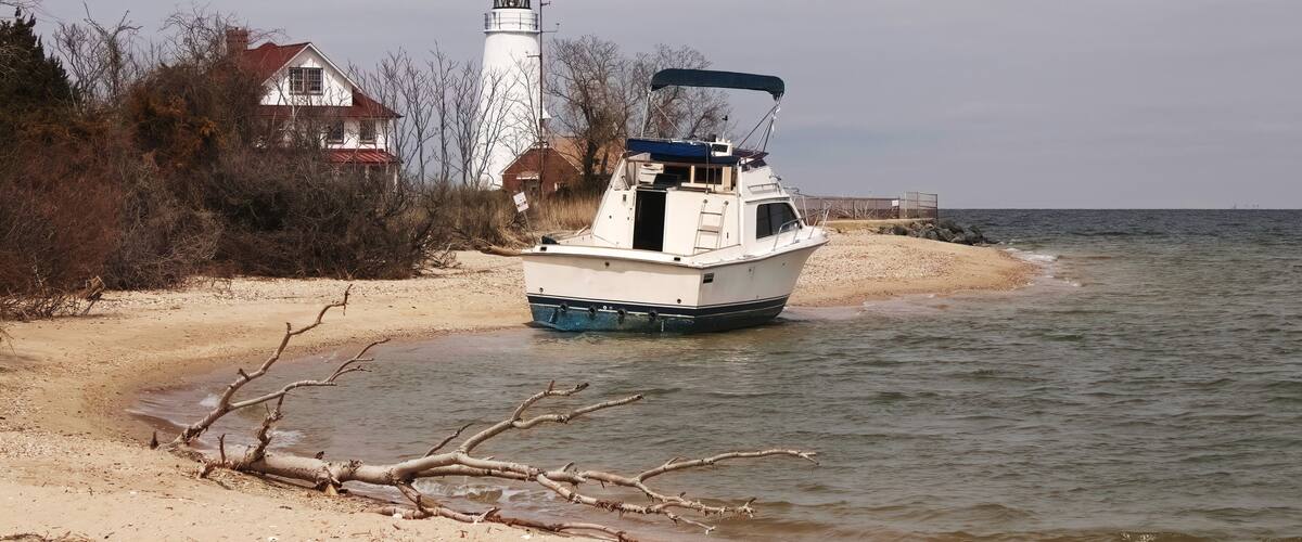 A boat on a sandy beach near a lighthouse.