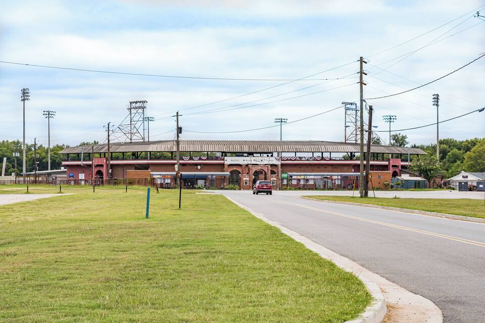 A large sports stadium with a red brick facade, multiple entrances, and a parking lot.