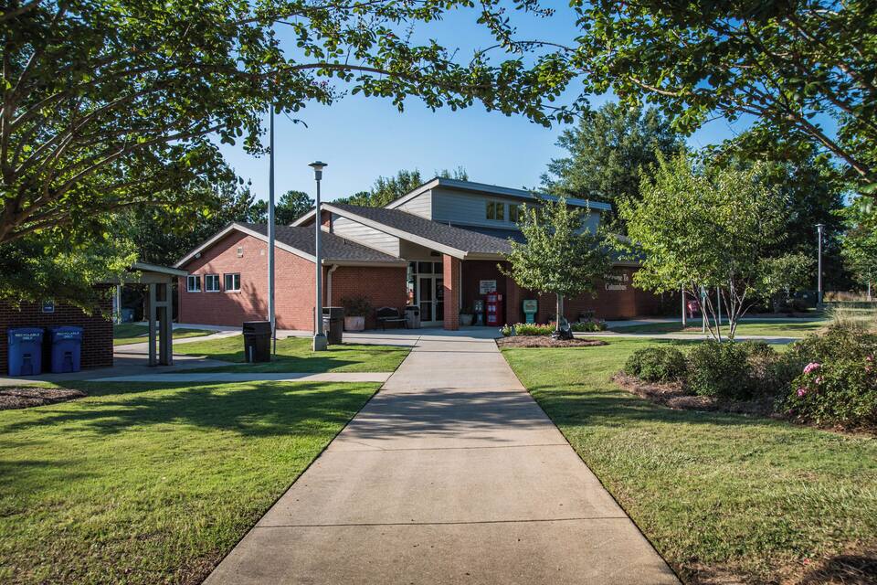 A brick building with a red door, a sidewalk, and green trees.