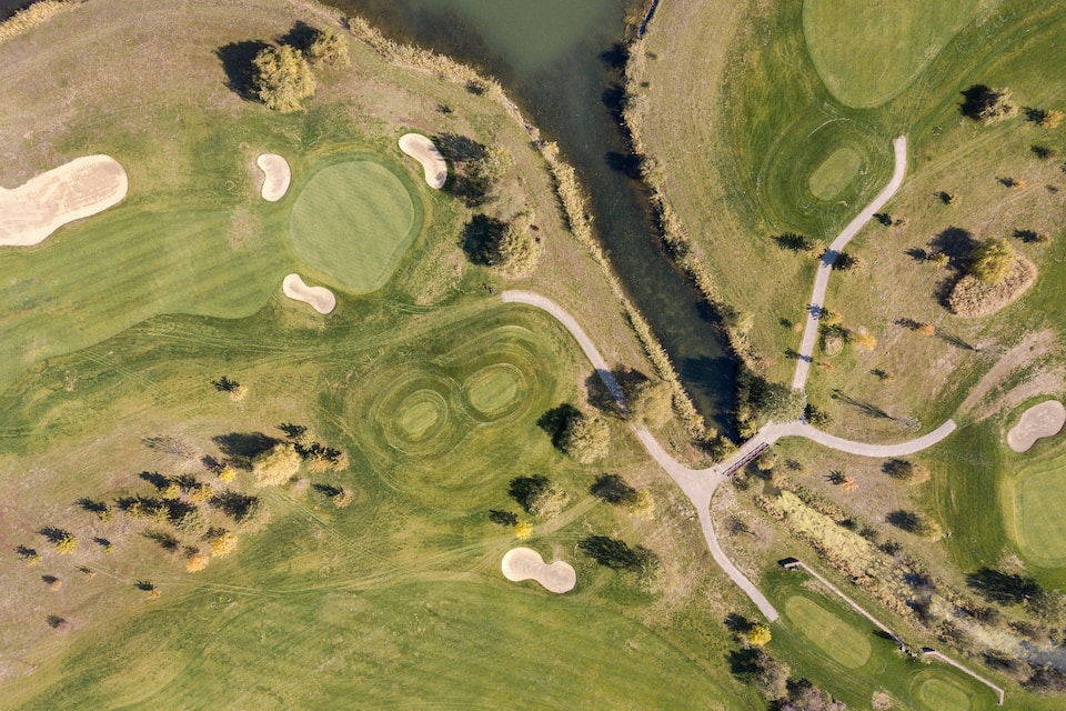 Vue aérienne d’un parcours de golf avec des bunkers de sable, des obstacles d’eau et un pont.