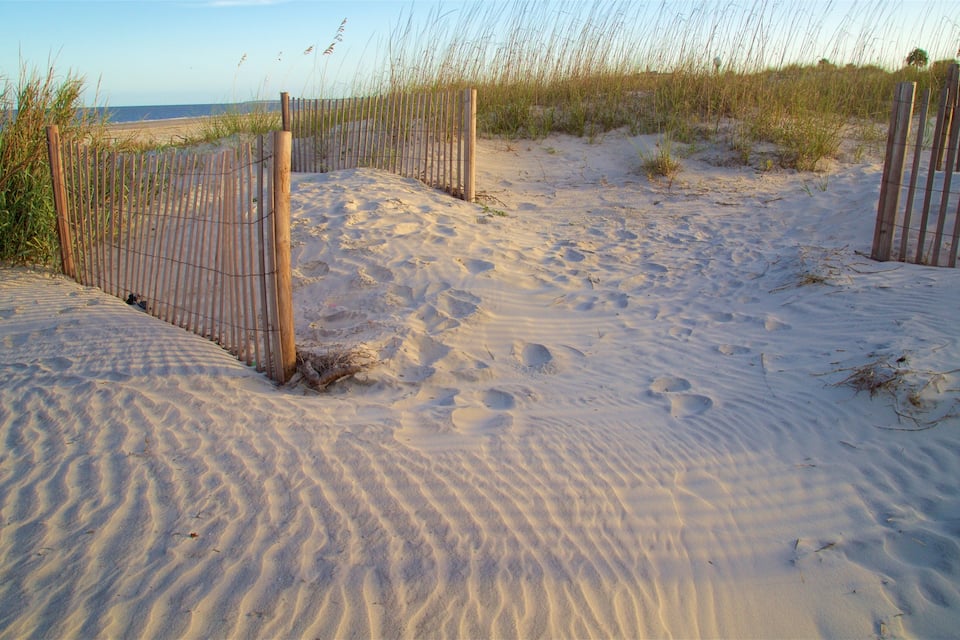 A sandy beach with footprints and a wooden fence.