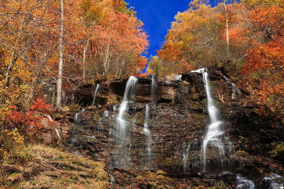 A waterfall cascading over a rocky cliff surrounded by autumn-colored trees.