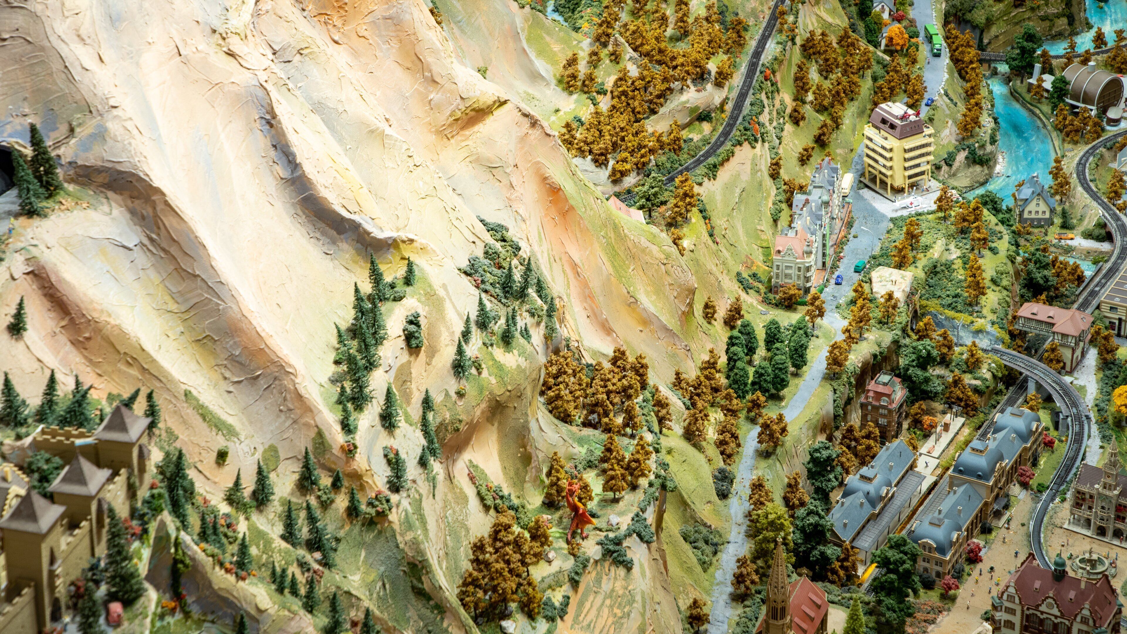 A detailed model of a mountainous landscape with a river, railway, and various buildings.