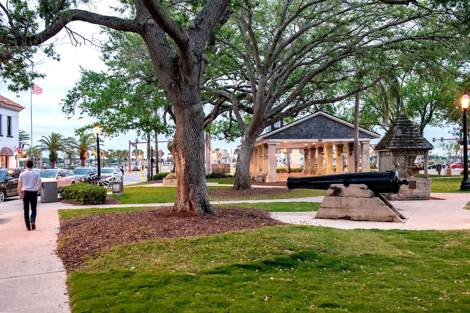 Um parque com uma grande árvore, um coreto e um canhão.