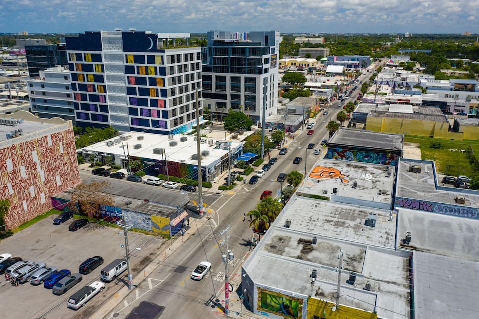 Una calle urbana con edificios modernos, coches estacionados y un cielo despejado.