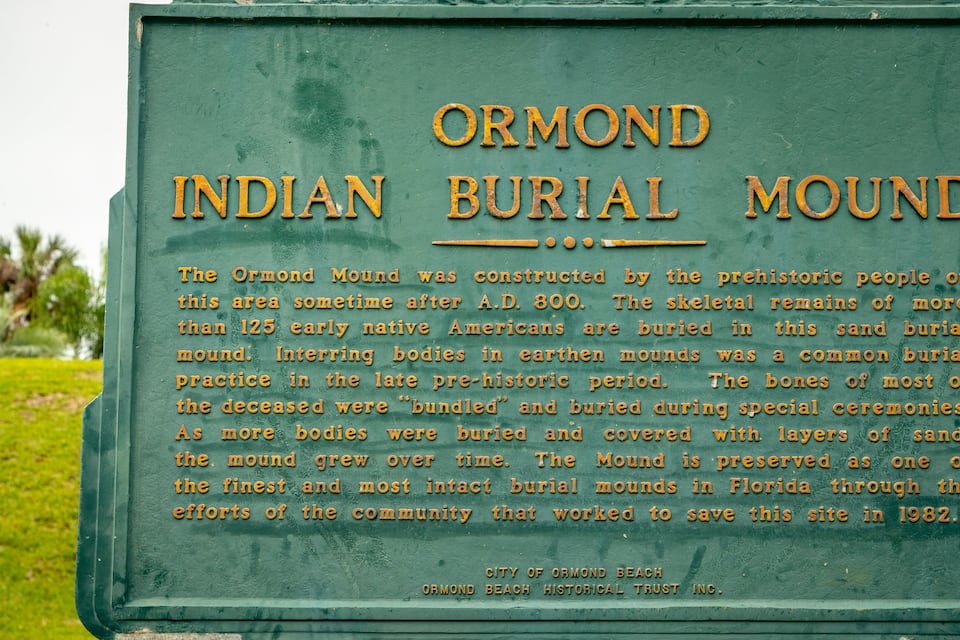 Et grønt skilt med teksten "Ormond Indian Burial Mound" og en beskrivelse af dets historiske betydning.