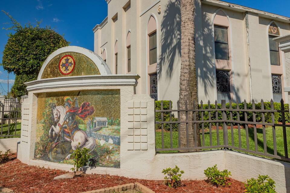 A building with a mosaic mural, a fence, and a tree.