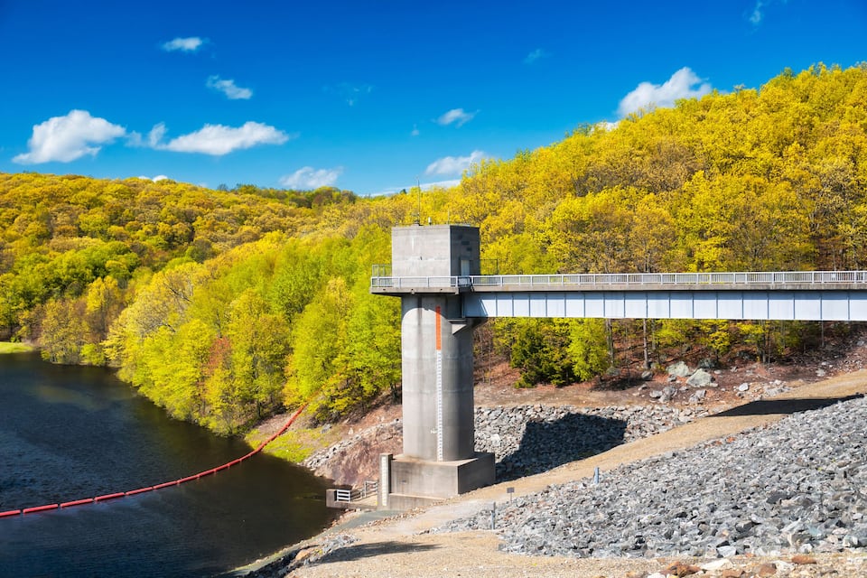 Een betonnen brug over een rivier, met een bebost heuvellandschap op de achtergrond.