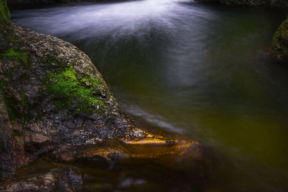 A waterfall flowing over moss-covered rocks in a forested area.