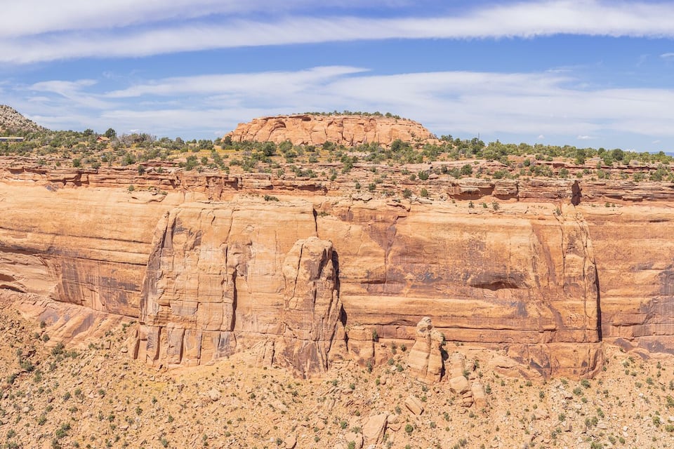 A large red rock cliff with a flat top and a small hill in the background.