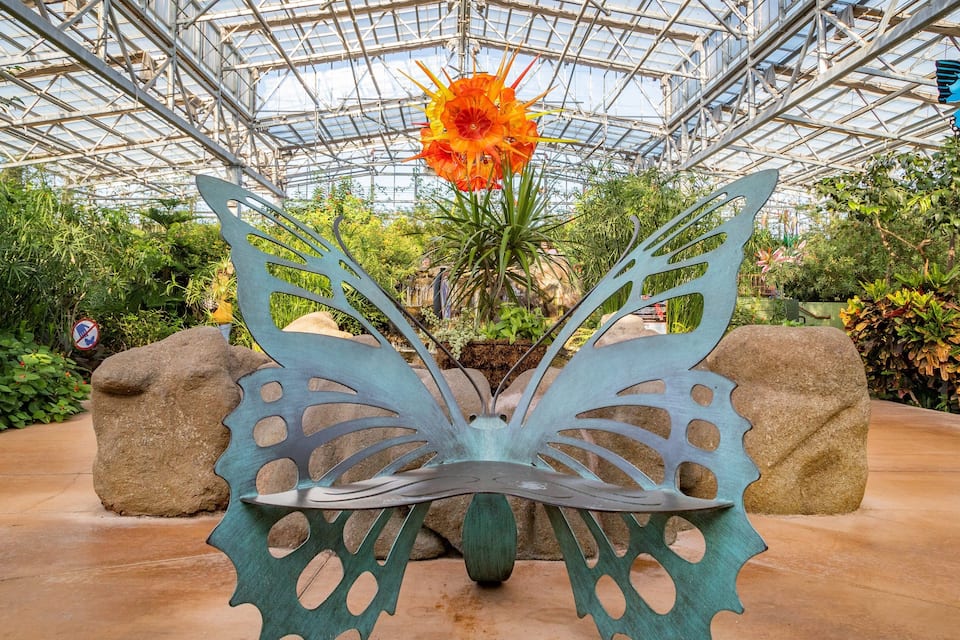 A greenhouse with a metal sculpture of a butterfly and a flower.