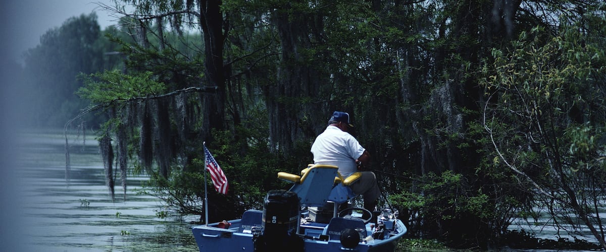 A man in a boat with an American flag, surrounded by water and trees.