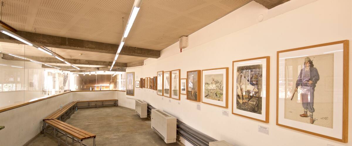 An art gallery with framed artworks on the walls and benches along the sides.