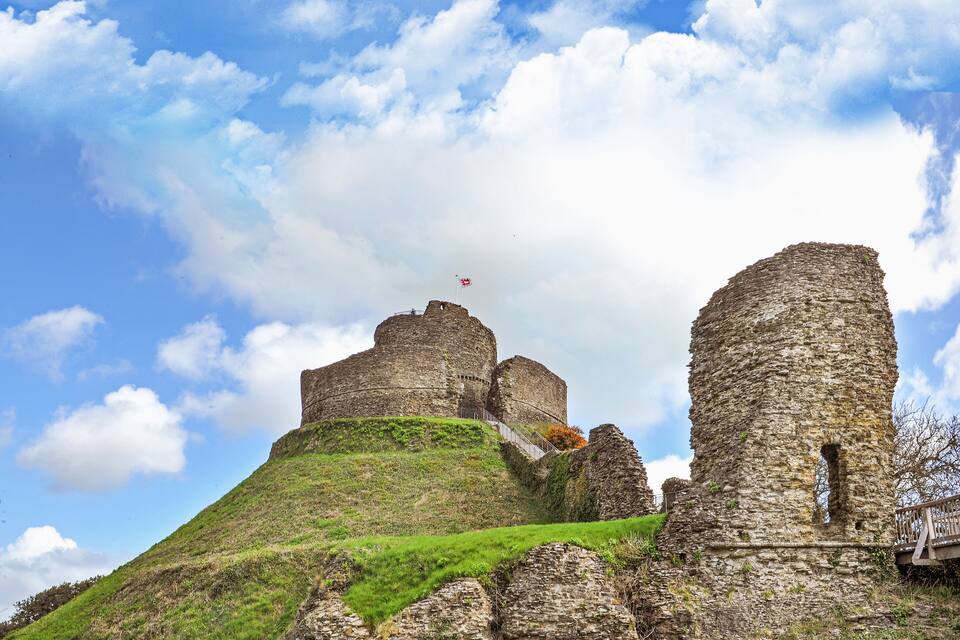 Un castell de pedra històric sobre un turó verd amb un cel serè.