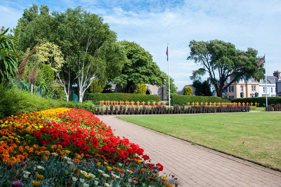 A landscaped garden with a variety of colorful flowers, a brick pathway, and several large trees.