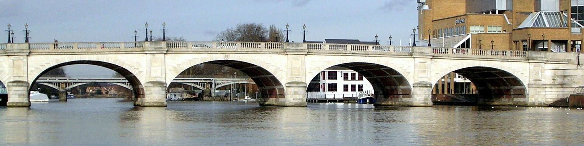 A river with swans swimming, a bridge with multiple arches, and a building with solar panels.
