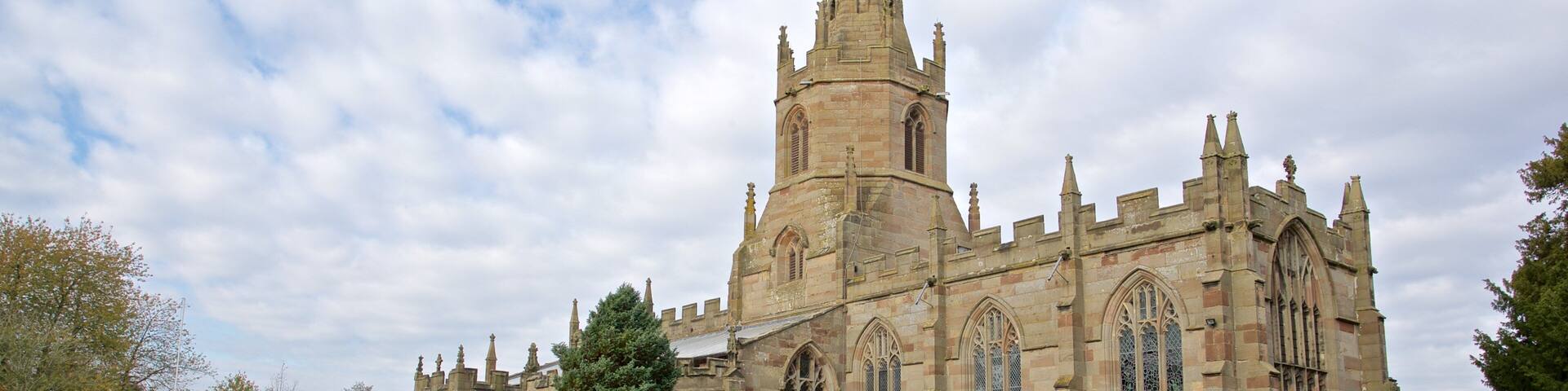A historic church with a tall spire and Gothic architecture, surrounded by a cemetery with headstones and flowers.