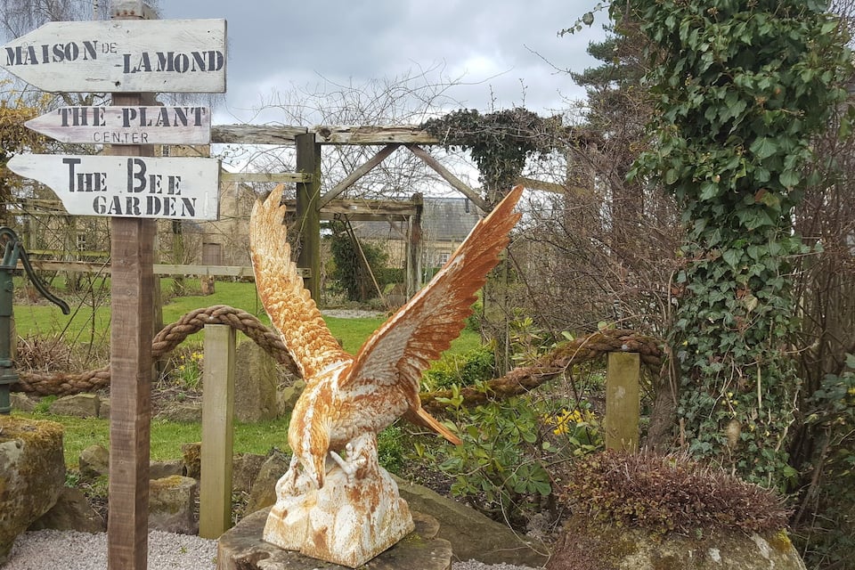 Un panneau indicateur en bois indiquant les directions vers « The Plant Center », « The Bee Garden » et « Maison de Lamond ».
