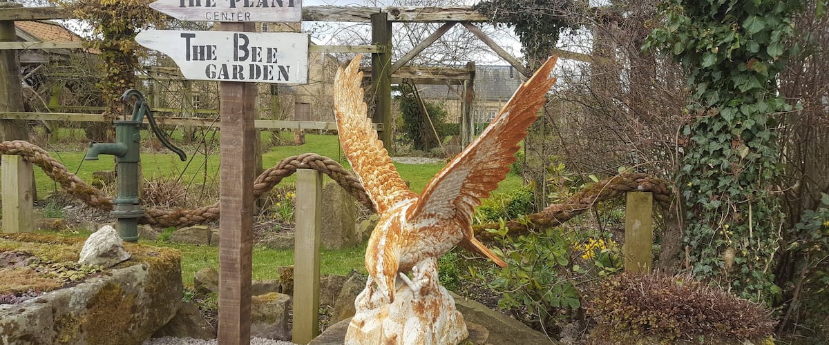 A wooden signpost with directions to 'The Plant Center', 'The Bee Garden', and 'Maison de Lamond'.