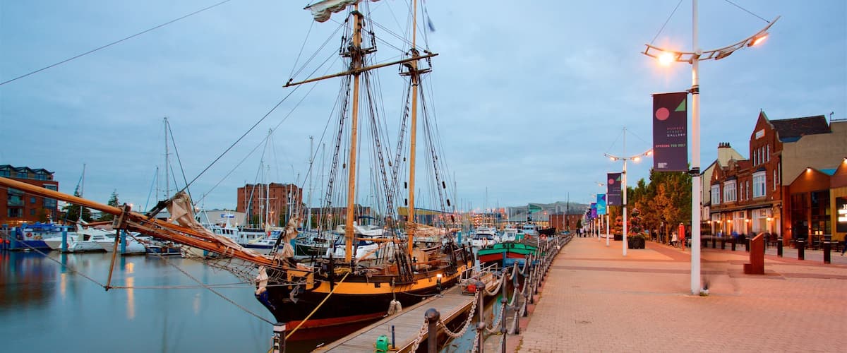 A historic sailing ship docked at a marina with a waterfront promenade and buildings in the background.