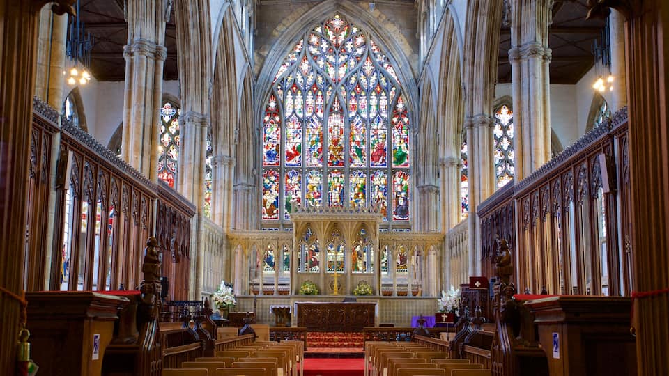 Interior de una catedral con un amplio vitral, bancos de madera y arquitectura gótica.