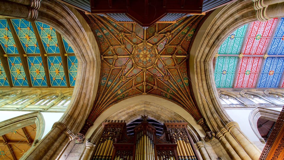 Interior de una catedral con vidrieras ornamentales, un techo de madera detallado y un órgano tubulado.