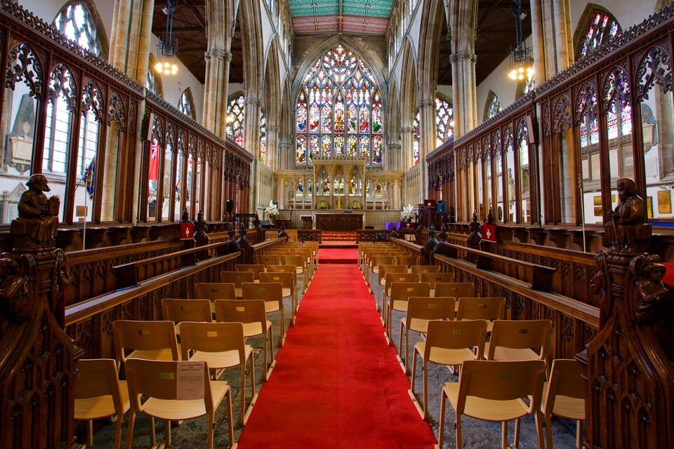 A church interior with wooden pews, a red carpet, and stained glass windows.