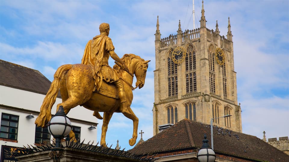 Una estatua dorada de un hombre a caballo, una torre del reloj y un edificio con una cruz en la parte superior.