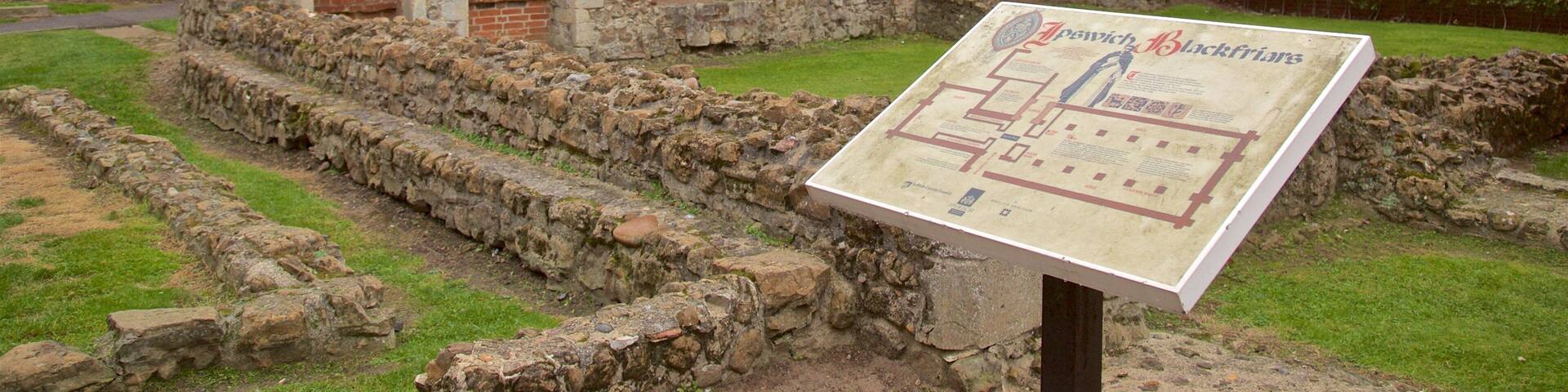 Ruinas antiguas con arcos de piedra, un muro de piedra y un cartel.