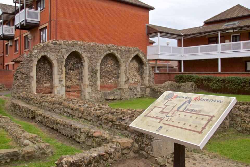 Ancient ruins with stone arches, a stone wall, and a signboard.
