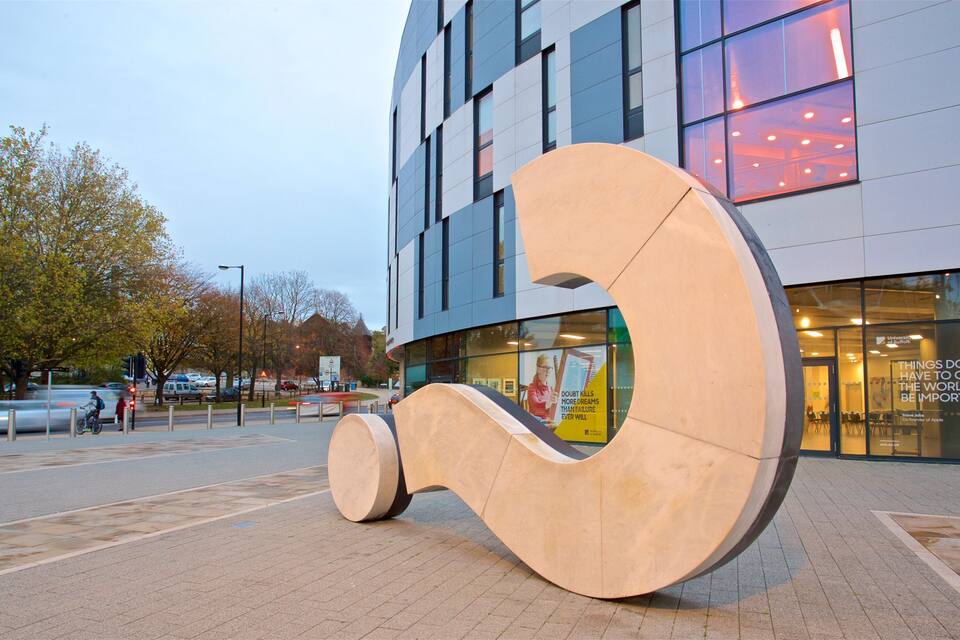 A modern building with large windows and a large, abstract sculpture in front.