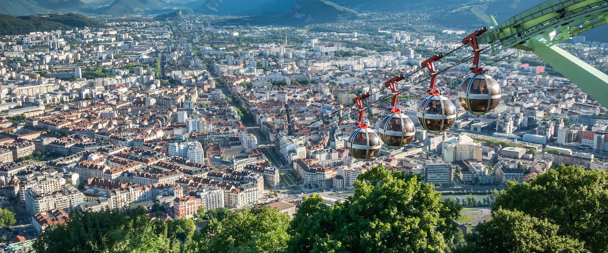 Une vue urbaine avec un réseau de téléphériques, des montagnes en arrière-plan et un ciel dégagé.