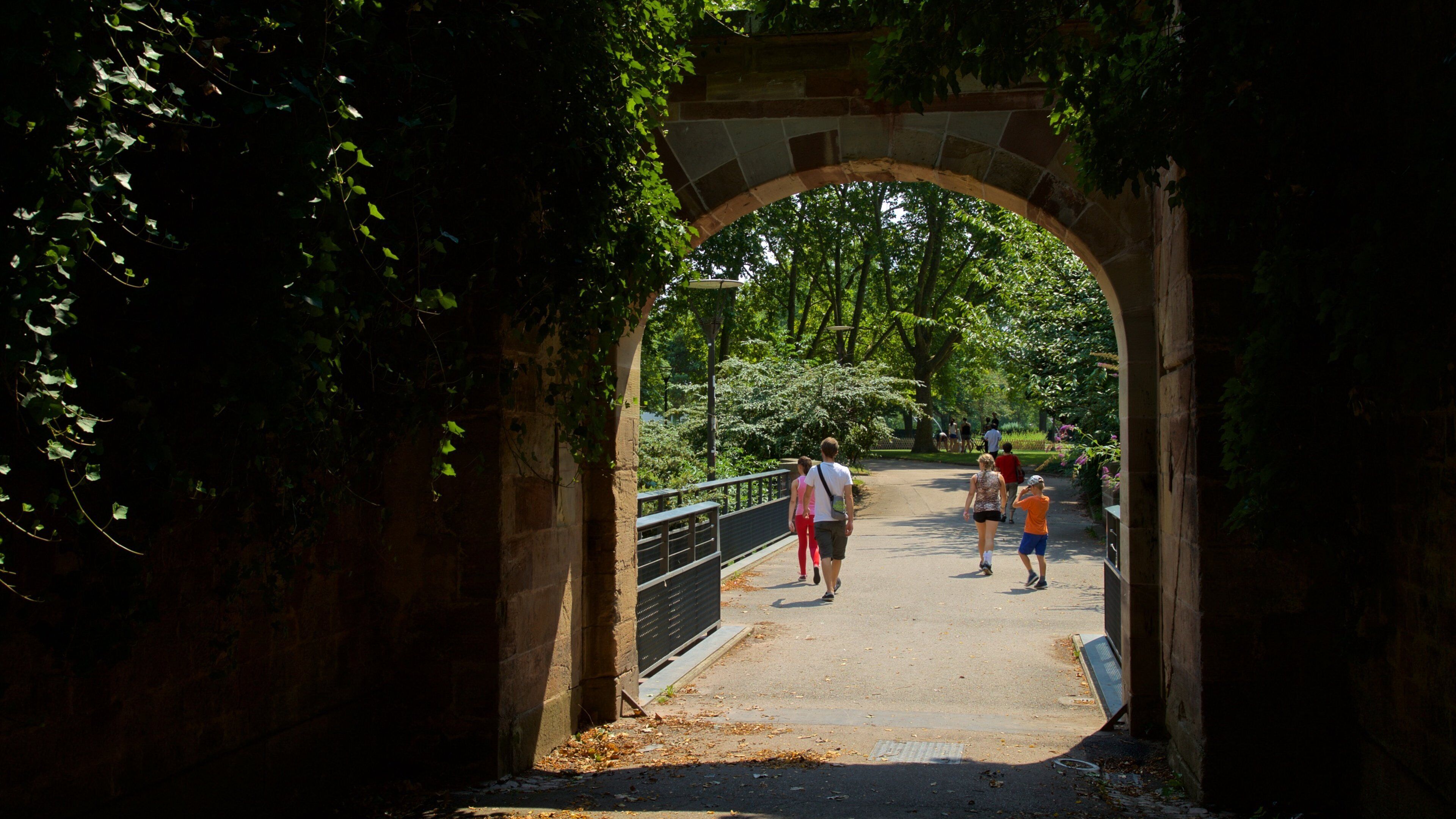 An archway with greenery on either side, leading to a pathway with people walking.