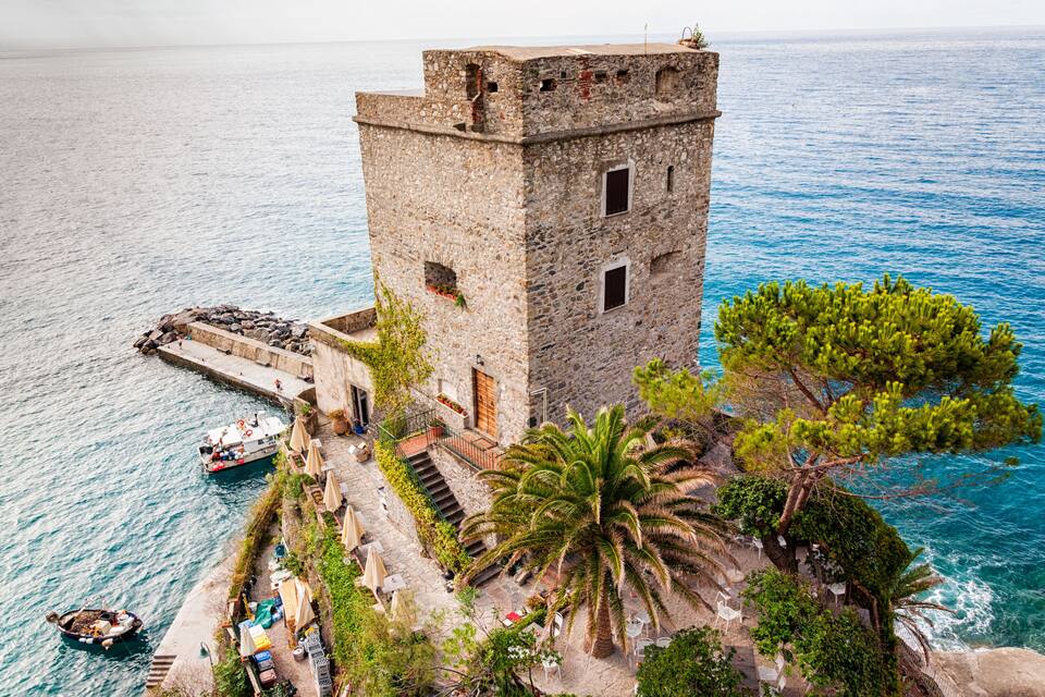 A coastal tower with a staircase leading up to it, surrounded by palm trees and a small boat in the water.