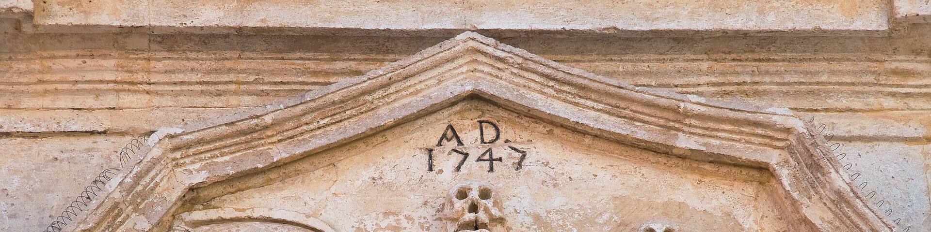 Un grabado en piedra con dos esqueletos y una figura central, datado en 1747 d.C.