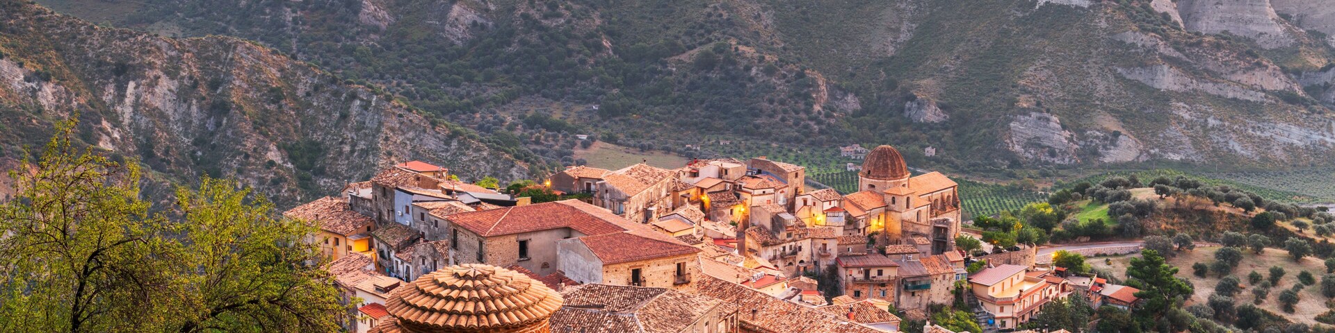 A village with traditional architecture nestled in a valley, surrounded by cliffs and olive groves.