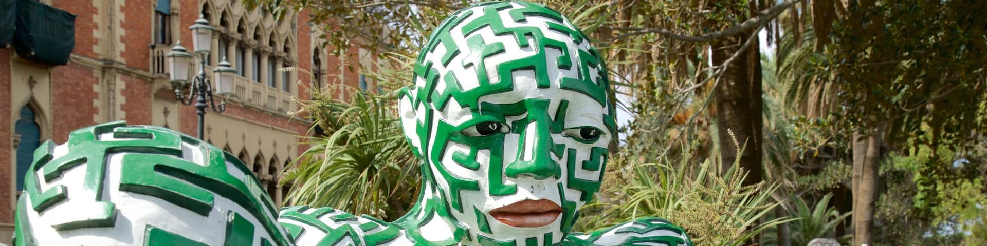 A person with a green and white maze pattern on their body, standing in a park with trees and a building in the background.
