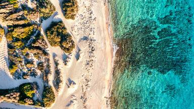 An aerial view of a beach with clear turquoise waters, sandy shore, and rocky outcrops.