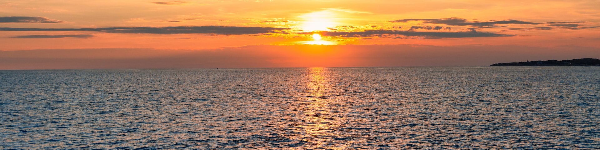 A sunset over the ocean with a rocky shoreline.