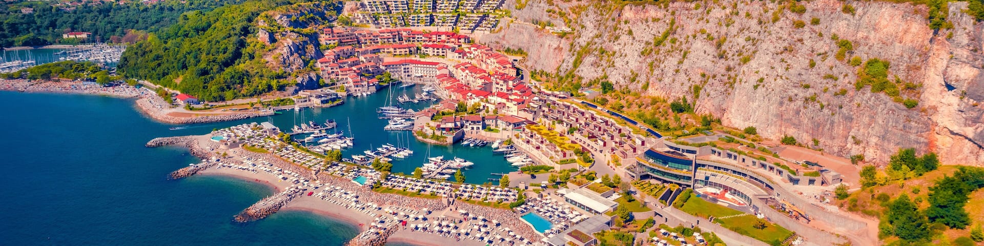 A coastal town with a marina, a large pool area, and a cliffside.