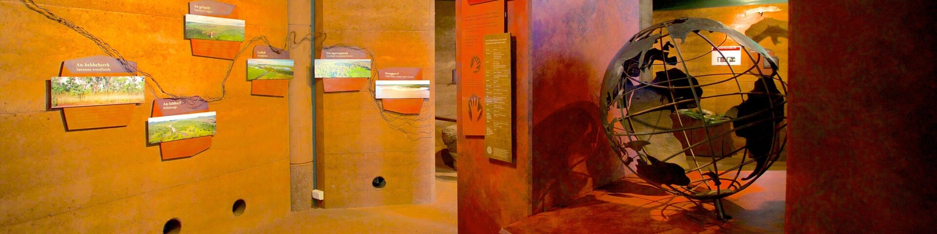 Una exposición interior con paredes anaranjadas, un globo terráqueo y paneles informativos.