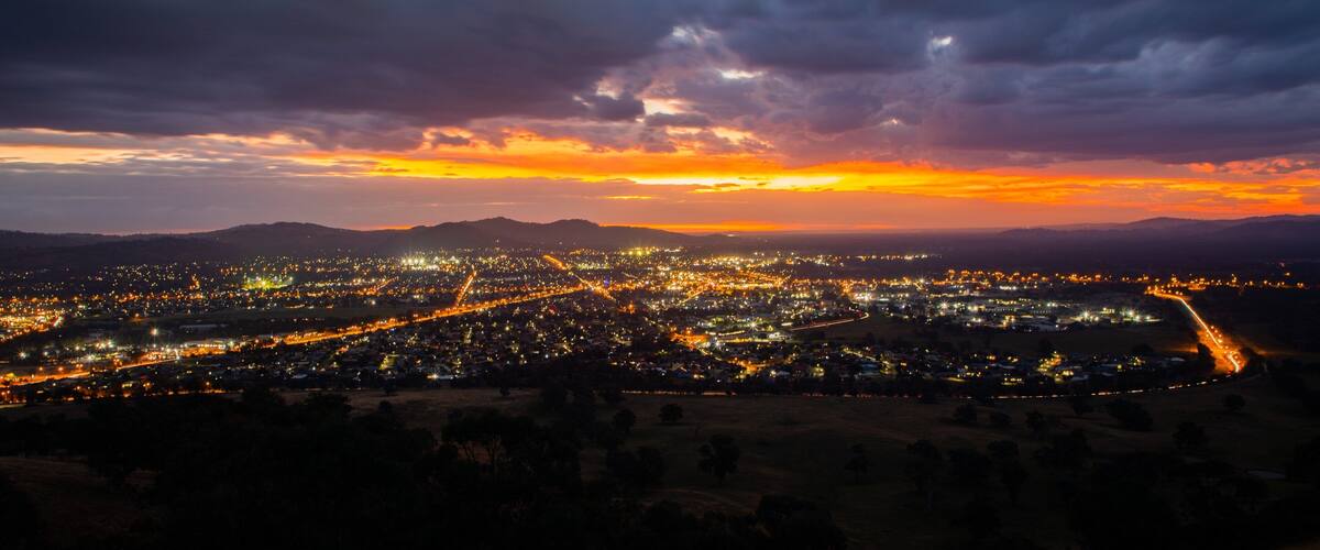 A city at dusk with a sunset over mountains.