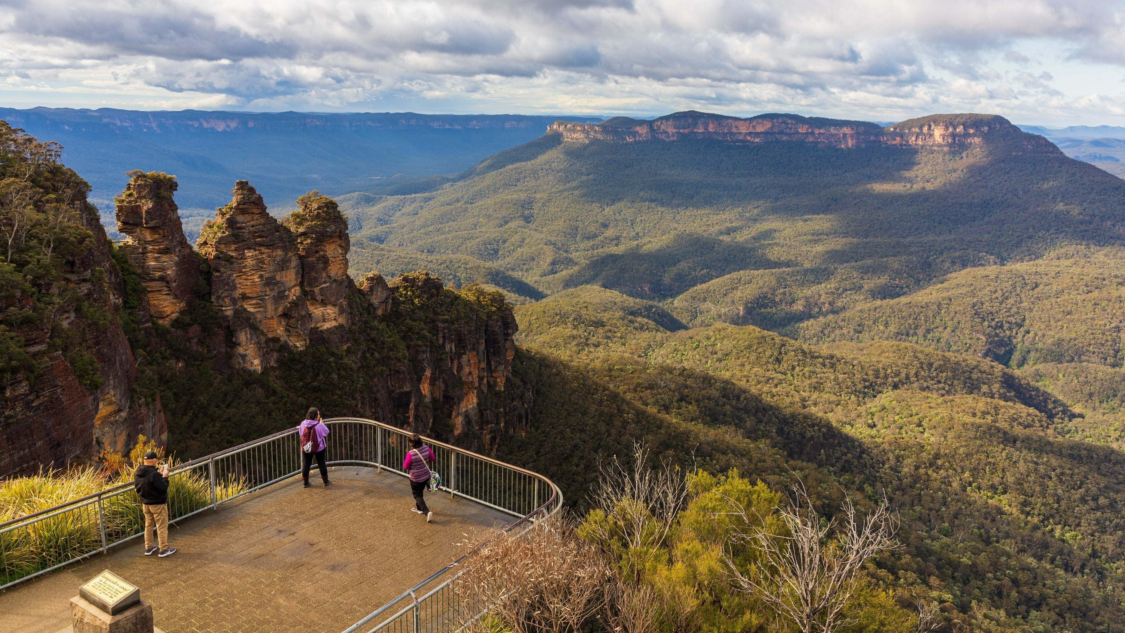A scenic overlook with a metal railing, rocky cliffs, and a vast forested valley.