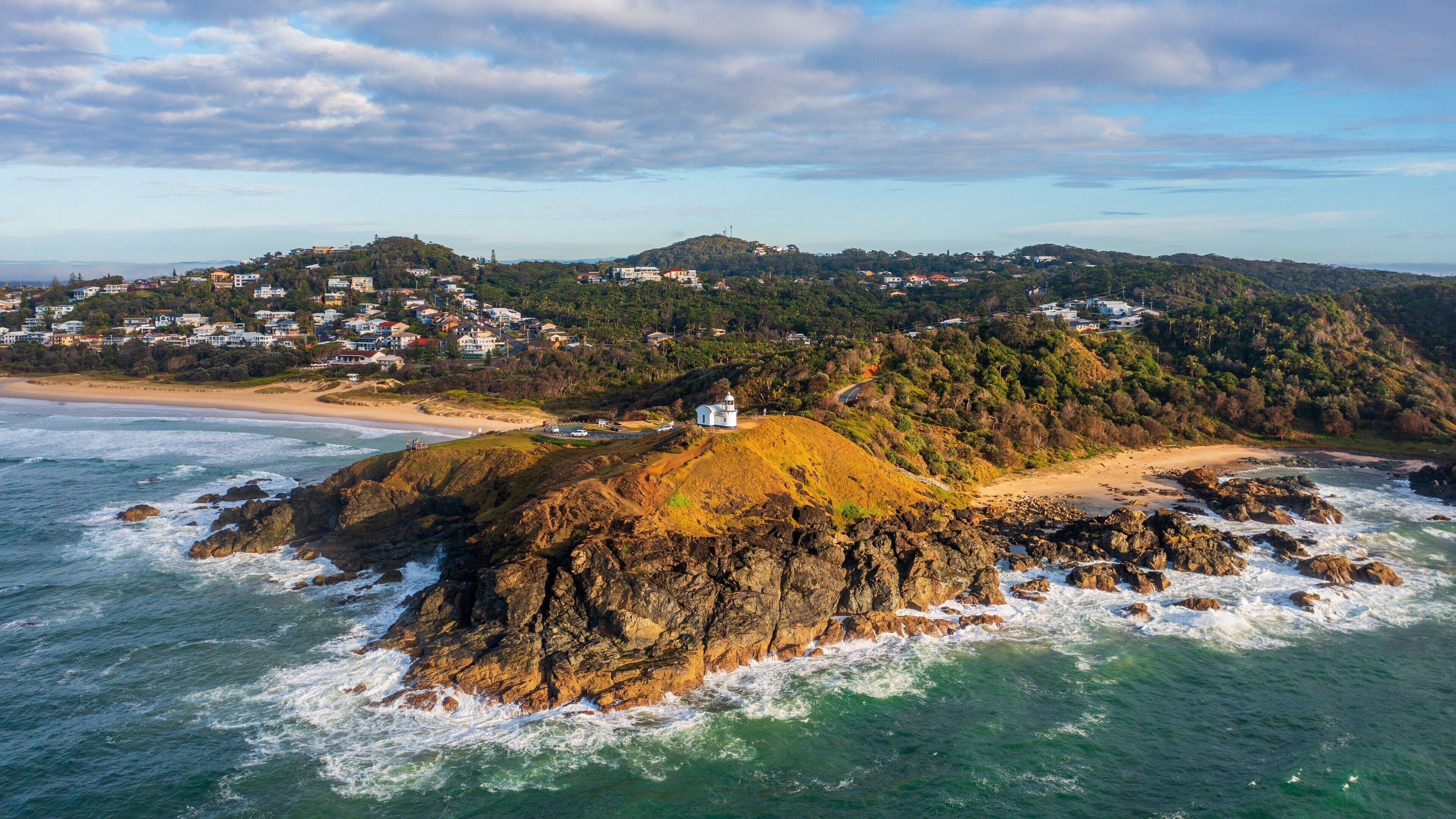 A coastal town with a lighthouse on a rocky outcrop, surrounded by hills and a beach.