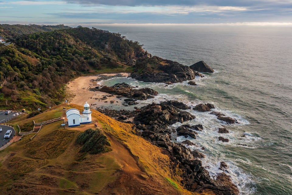 A coastal landscape with a lighthouse, rocky shoreline, and a road curving along the coast.