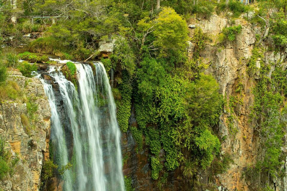 A multi-tiered waterfall surrounded by dense greenery and rocky cliffs.