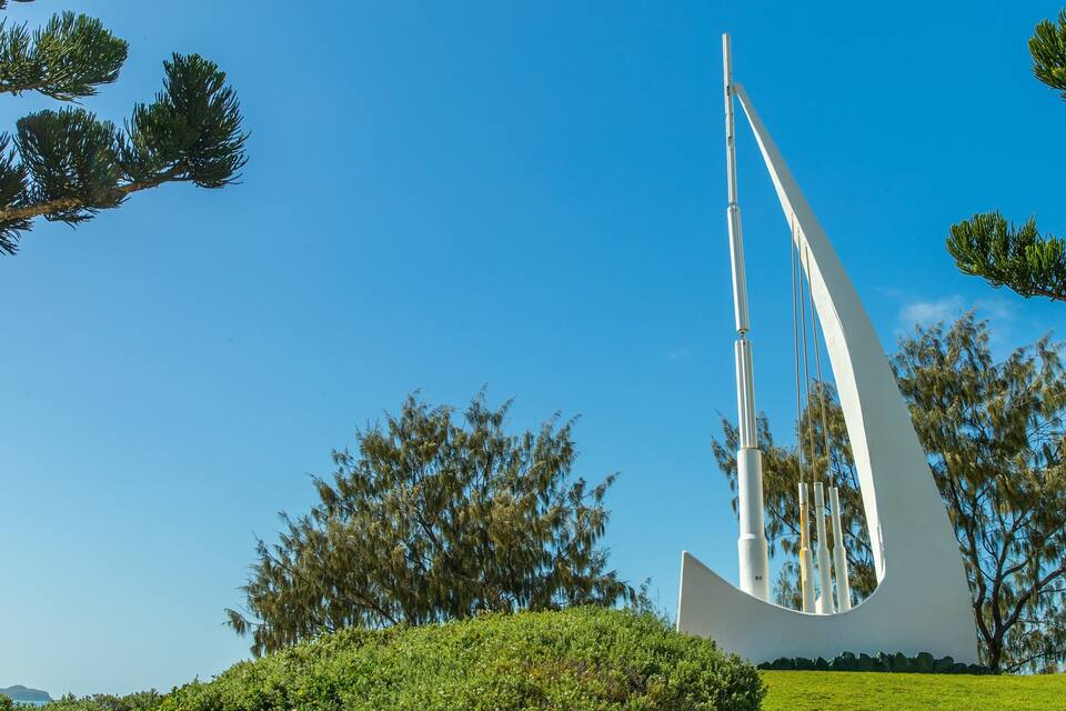 A modern sculpture in a park with green grass and trees.