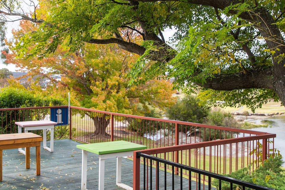 A wooden deck with tables and a railing overlooking a lake.