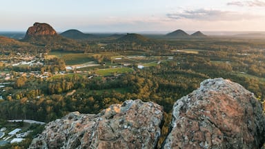 A mountainous landscape with a prominent rocky outcrop in the foreground, a valley with agricultural fields, and distant hills.
